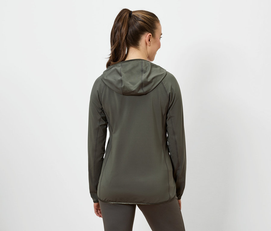 Frau mit braunen Haaren, die zu einem Pferdeschwanz zusammengebunden sind, trägt eine olivgrüne Jacke mit Kapuze und olivgrüne Leggings.