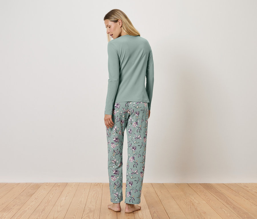 Frau steht mit dem Rücken zur Kamera und trägt einen hellgrünen Pyjama mit langen Ärmeln und einer geblümten Hose.