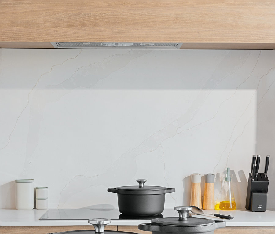 Drei schwarze Töpfe mit Deckeln auf einer weißen Küchentheke. Auf einem Schneidebrett liegen Tomaten und Kartoffeln.