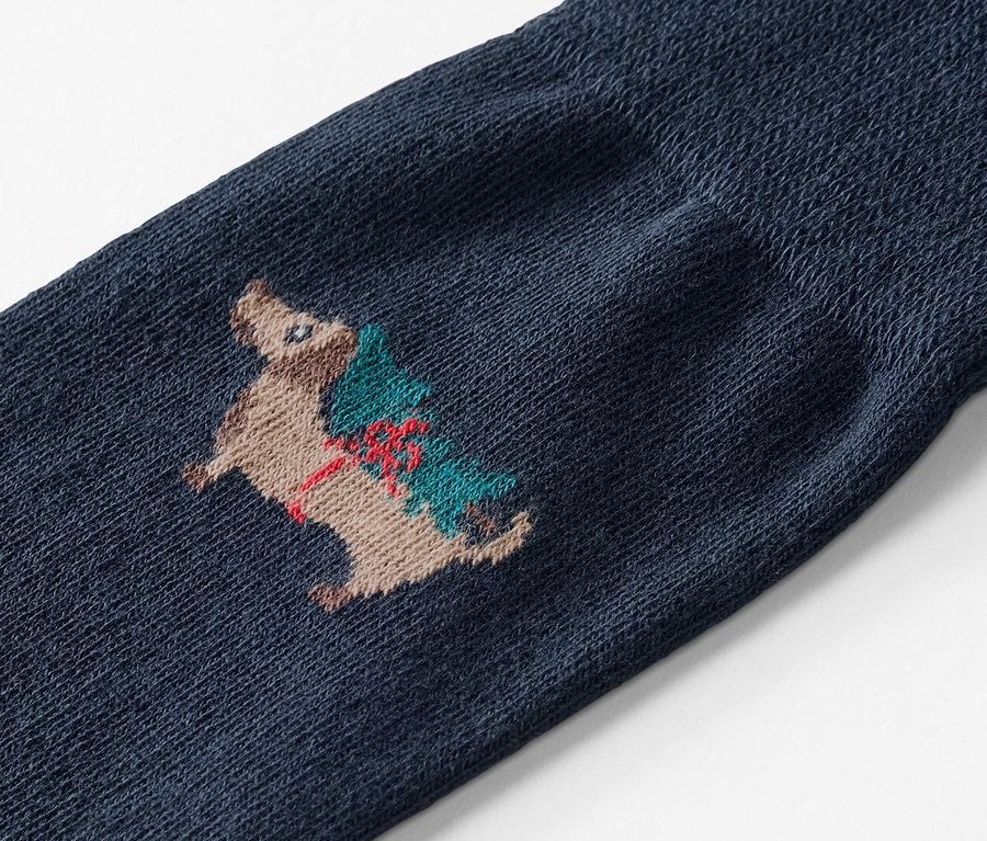 Detailaufnahme einer blauen Socke mit der Stickerei eines Igels, der einen Weihnachtsbaum trägt.