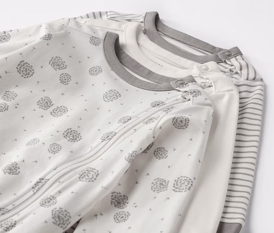 Drei Baby-Pyjamas mit Löwenzahn- und Streifenmuster.