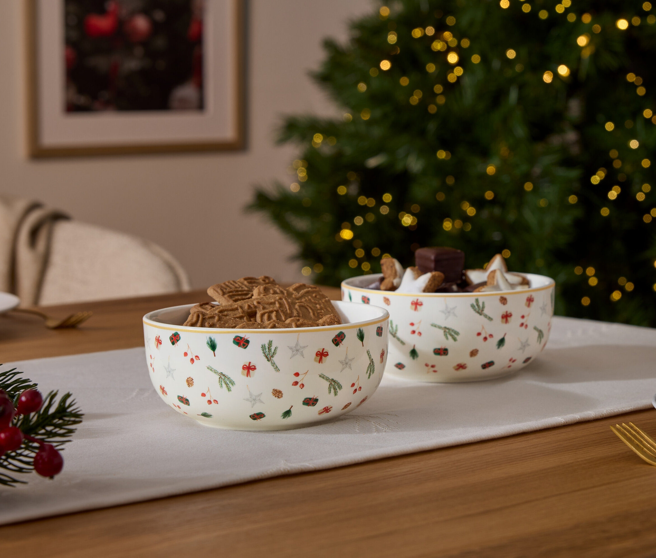 Zwei Schüsseln mit Weihnachtsmotiven, eine gefüllt mit Lebkuchen, die andere mit Schokolade und Sternen, auf einem Tisch mit Weihnachtsdekoration.