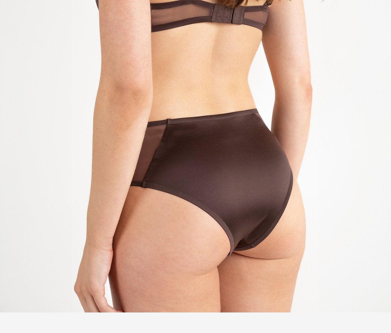 Frau von hinten, die einen dunkelbraunen BH und einen Passionata High Waist Slip »Bianca« in Dunkelschokolade mit transparenten Seiteneinsätzen trägt.