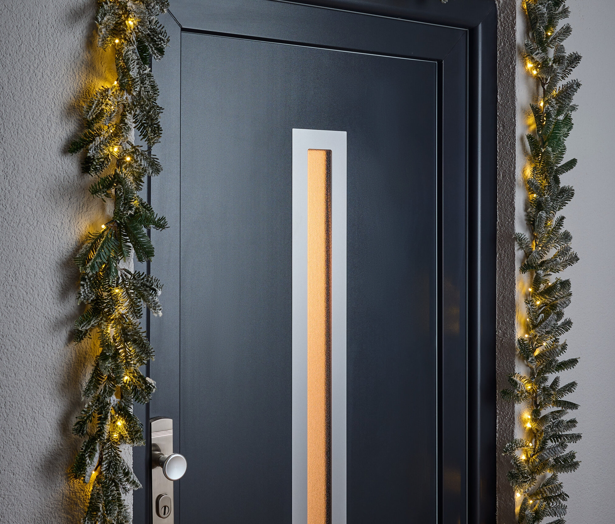Eine schwarze Tür umrahmt von einer weihnachtlichen Girlande mit kleinen Lichtern.
