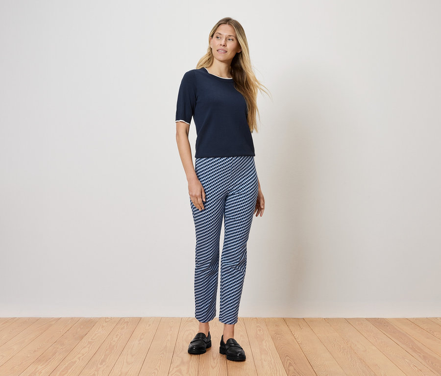 Eine Frau steht auf einem Holzboden und trägt ein dunkelblaues T-Shirt und blau-weiß gestreifte Hosen.