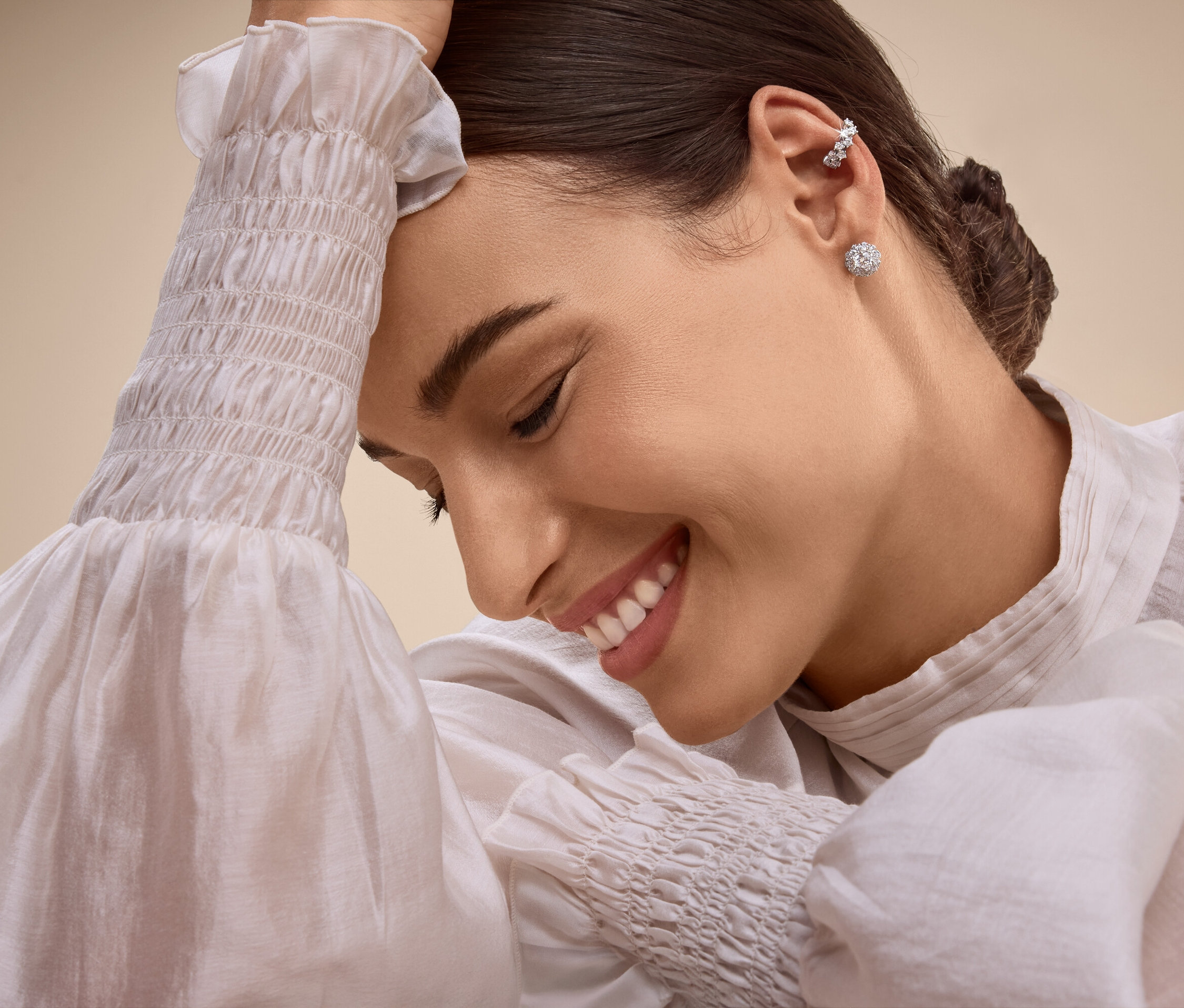 Lächelnde Frau mit Ohrringen und Ohrmanschette, die ihren Kopf mit der Hand stützt.