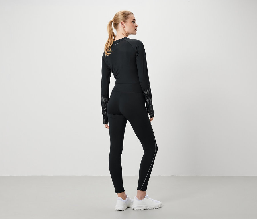 Eine Frau in schwarzer Sportbekleidung und weißen Schuhen steht mit dem Rücken zur Kamera.