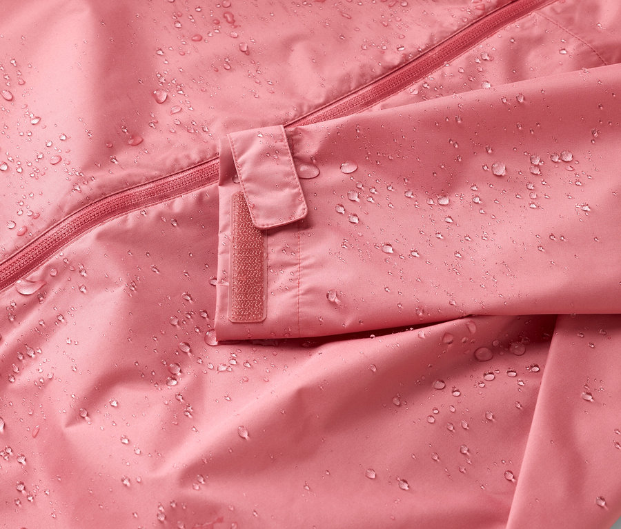 Nahaufnahme einer rosafarbenen Jacke mit Reißverschluss und Klettverschluss am Ärmel, bedeckt mit Wassertropfen.