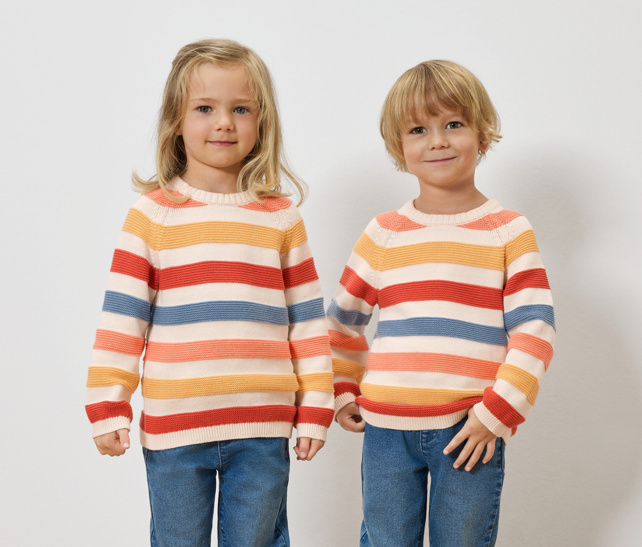 Zwei Kinder stehen nebeneinander und tragen gestreifte Pullover und Jeans.