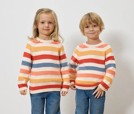 Zwei Kinder stehen nebeneinander und tragen gestreifte Pullover und Jeans.