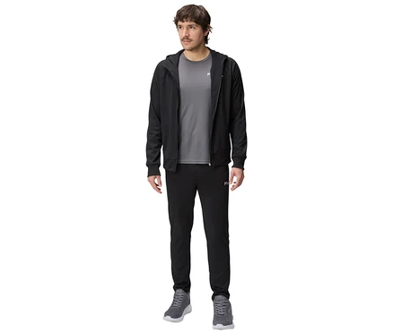 Mann in schwarzer Trainingsjacke mit Kapuze, grauem T-Shirt und schwarzer Trainingshose, dazu graue Turnschuhe.