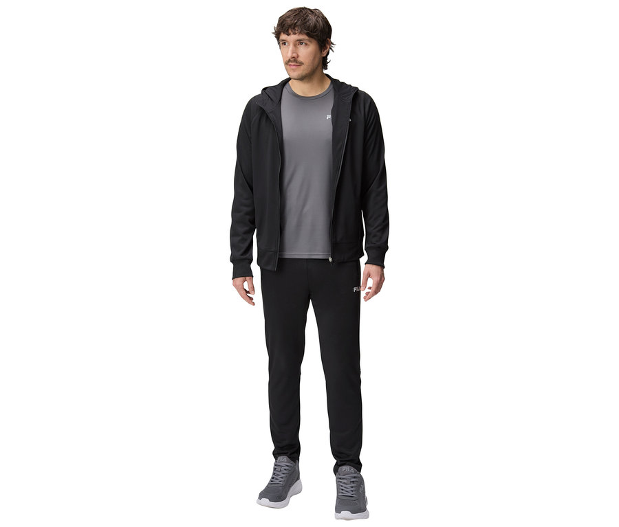 Mann in schwarzer Trainingsjacke mit Kapuze, grauem T-Shirt und schwarzer Trainingshose, dazu graue Turnschuhe.