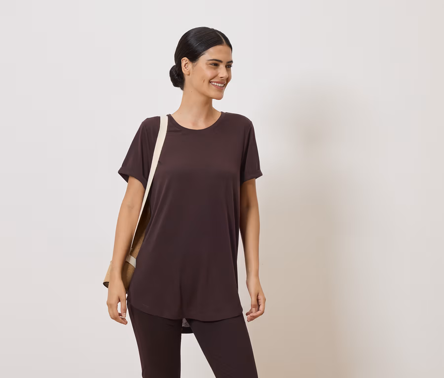 Frau mit Dutt trägt braunes T-Shirt und Leggings. Über der Schulter hängt eine beige Stofftasche.