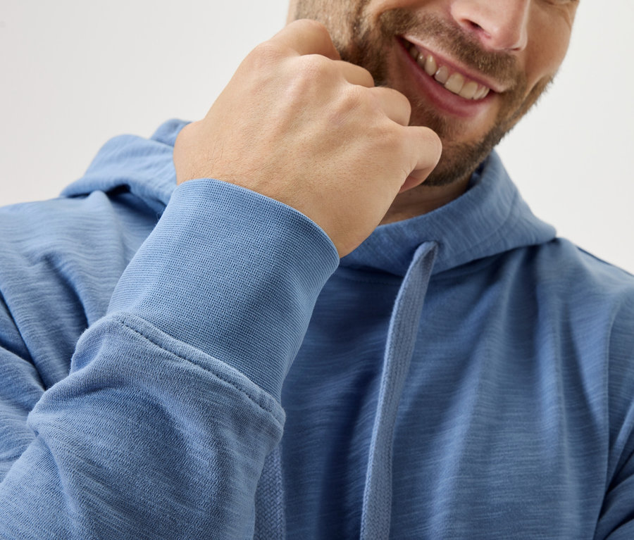 Lächelnder Mann mit blauem Hoodie berührt sein Kinn.