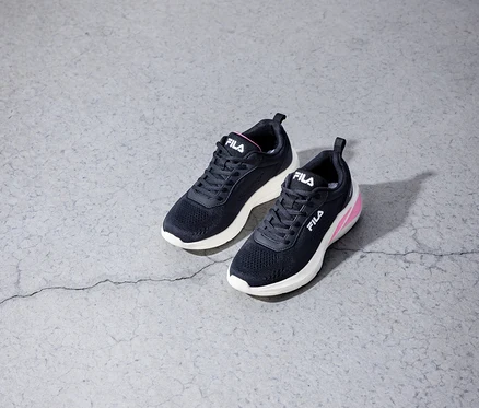 Zwei schwarze FILA Specctris Damen-Sneaker mit weißen Sohlen und pinken Akzenten liegen auf einem grauen Betonboden.
