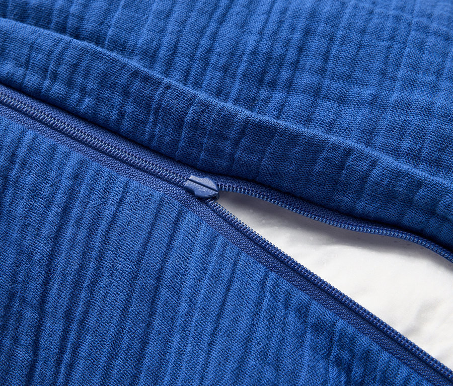 Nahaufnahme eines teilweise geöffneten, blau gefärbten Kissenbezugs mit Reißverschluss, der einen weißen Kisseninhalt freigibt.