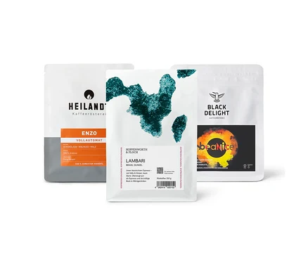 Drei Kaffeepackungen des "Vollautomaten Probierpaket "Caffè Crema Entdecker Set" - 3x 250 g Ganze Bohne" liegen auf einem Tisch.
