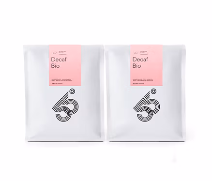 Zwei weiße Tüten Decaf Bio Kaffee mit rosa Etikett stehen nebeneinander vor einem weißen Hintergrund.