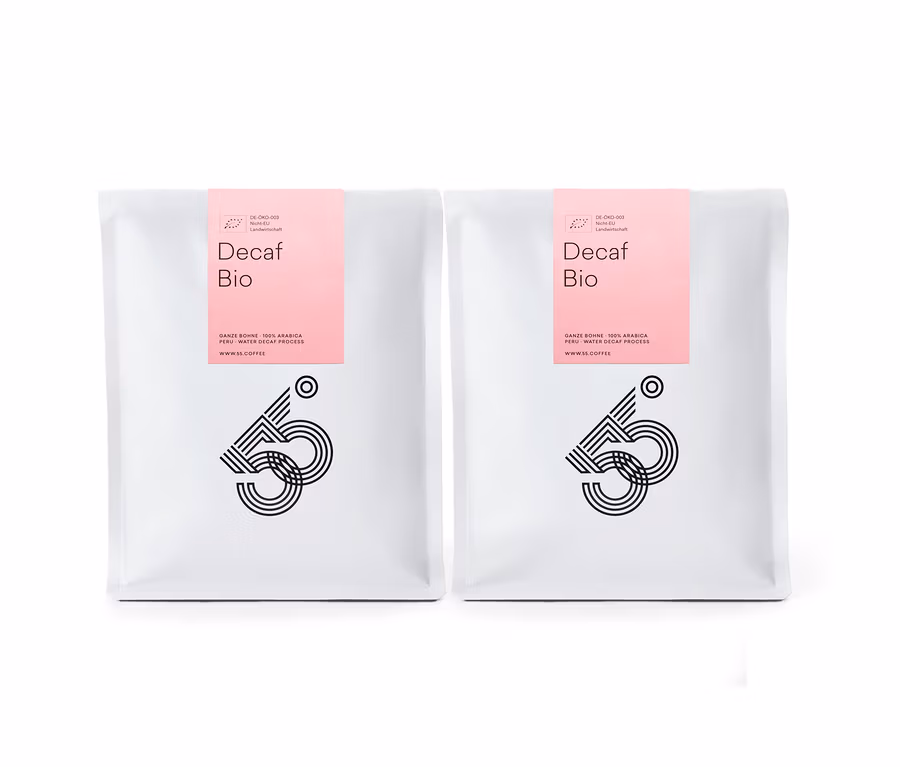 Zwei weiße Tüten Decaf Bio Kaffee mit rosa Etikett stehen nebeneinander vor einem weißen Hintergrund.