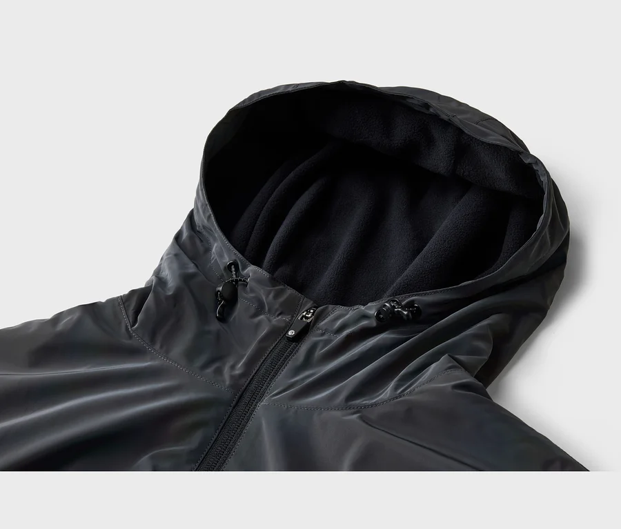 Nahaufnahme einer dunkelgrauen Jacke mit Kapuze, die mit schwarzem Fleece gefüttert ist. Die Jacke hat einen Reißverschluss und Kordelzüge mit Stoppern an der Kapuze.