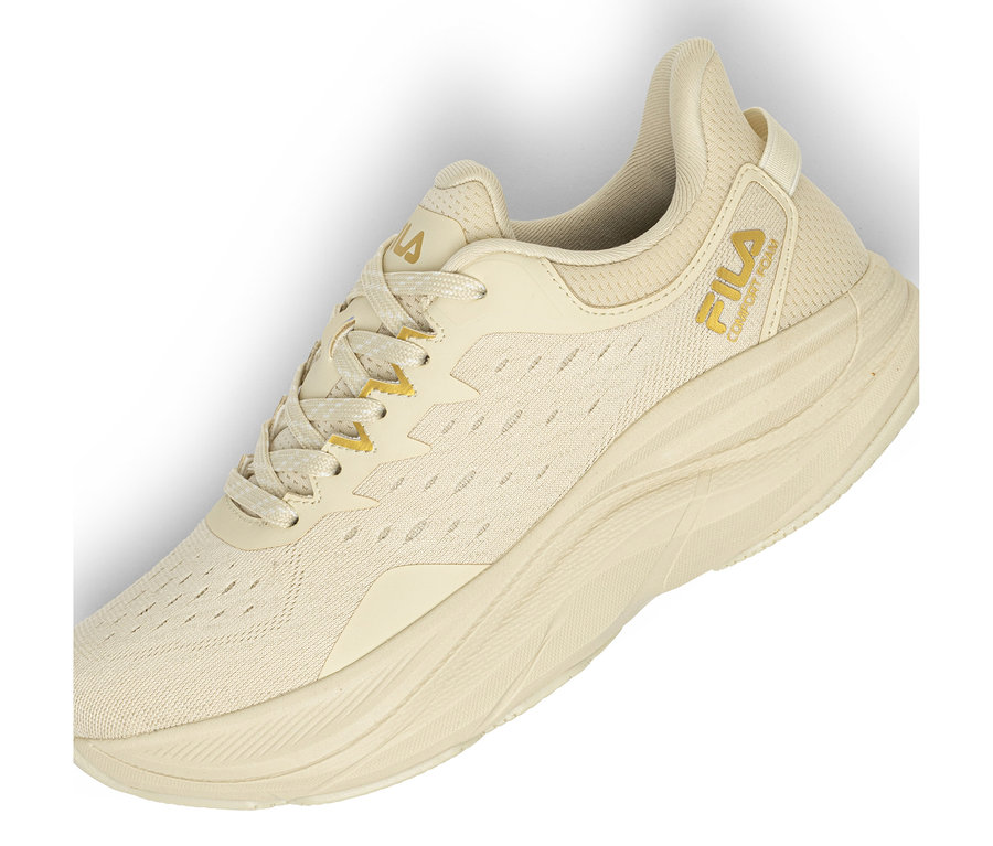 Ein einzelner hellbeiger Sneaker mit Mesh-Obermaterial und dicker, strukturierter Sohle. Ein goldenes Fila-Logo und der Schriftzug „COMFORT FOAM“ sind an der Seite sichtbar. Die Schnürsenkel sind beige mit goldenen Akzenten.