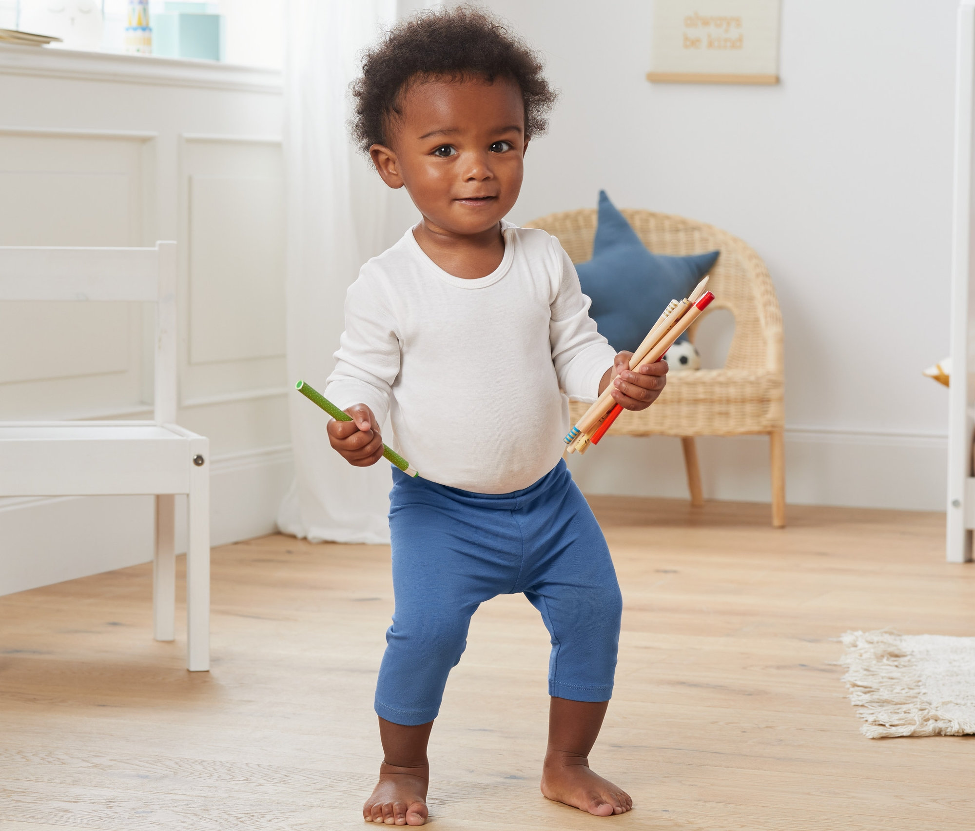 Ein Kind steht auf dem Boden und hält Buntstifte. Es trägt blaue 3/4-Leggings aus Bio-Baumwolle.