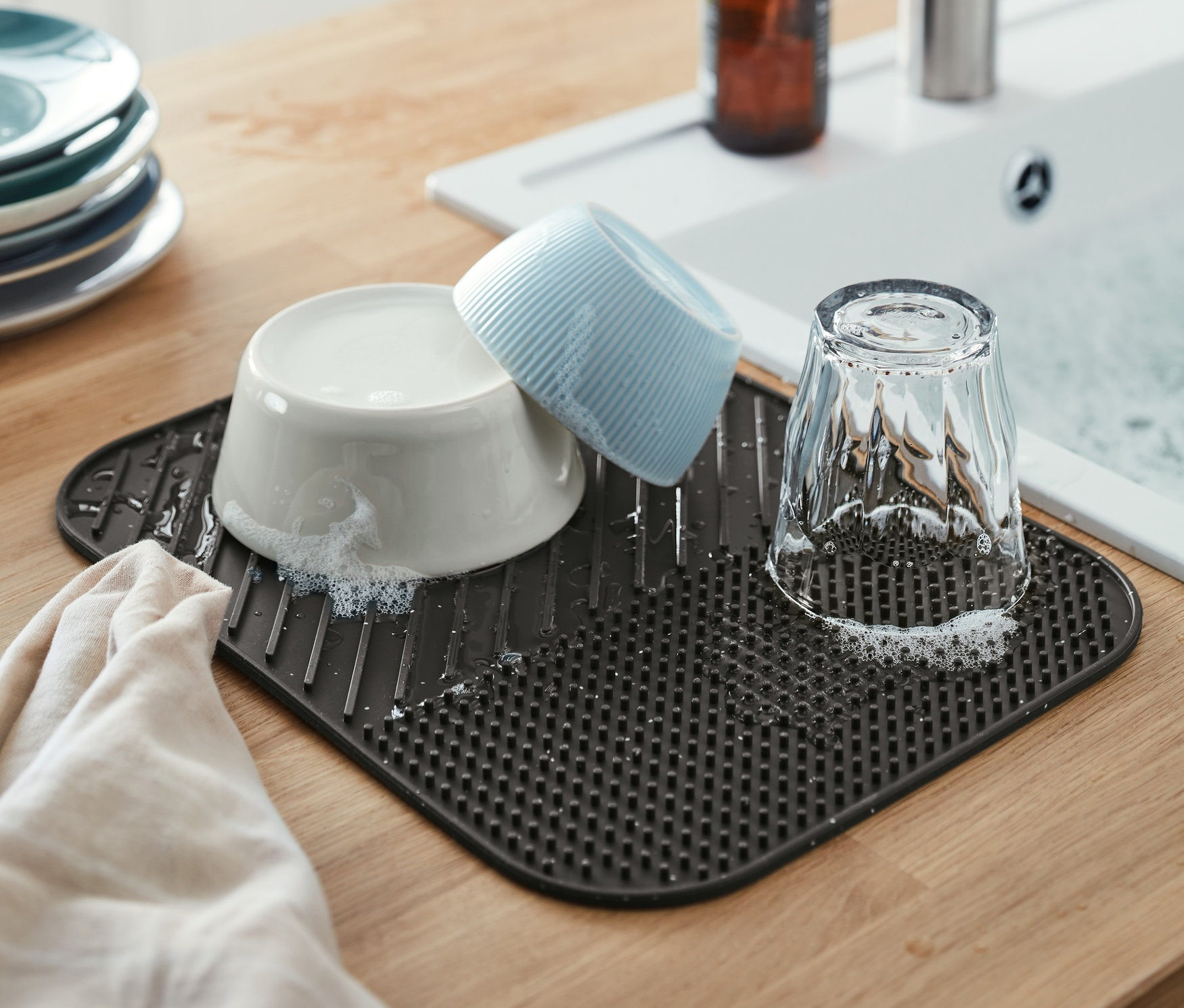 Eine graue Silikon-Abtropfmatte mit Geschirr neben einem Spülbecken.