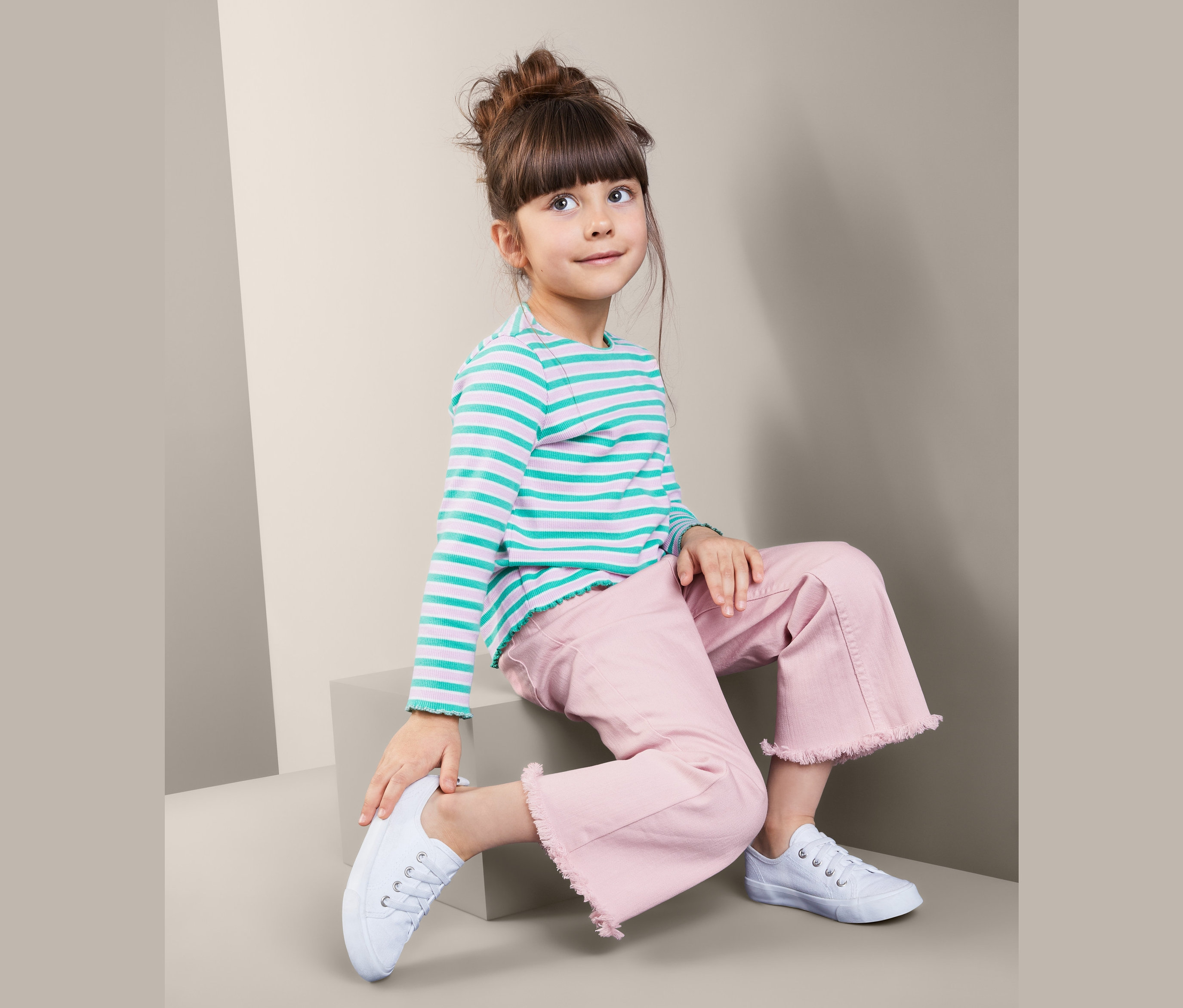 Mädchen sitzt auf Stufen mit Denim-Culotte, einem gestreiften Oberteil und weißen Turnschuhen.