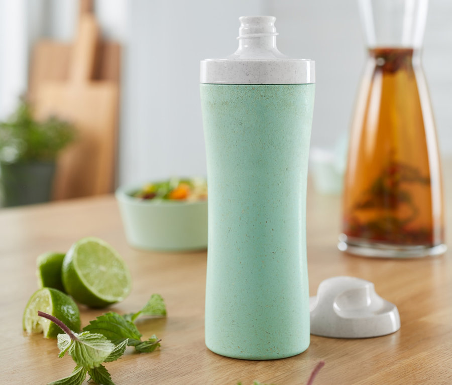 Eine grüne KOZIOL-Trinkflasche steht auf einem Holztisch neben Limetten und Minze.