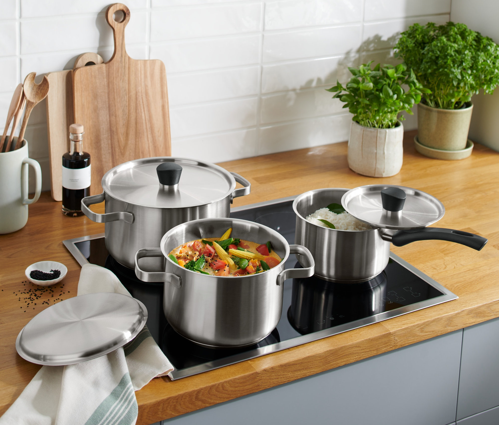 Edelstahl-Kochtopf-Set steht auf einem Induktionskochfeld, eines mit Gemüse, eines mit Reis.