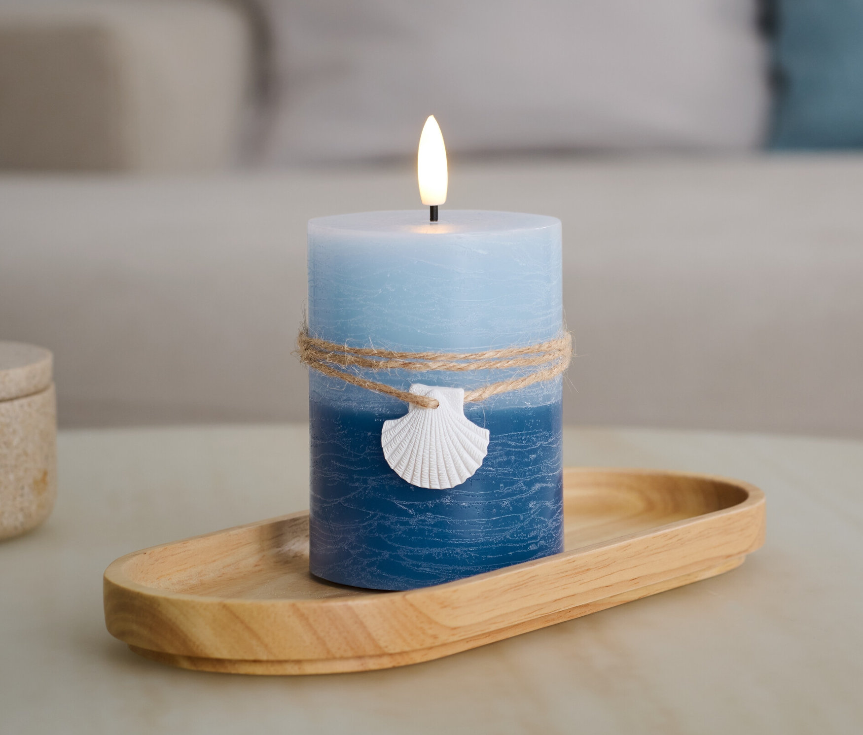 Eine blaue LED-Echtwachskerze »Muschel« steht auf einem Holztablett.