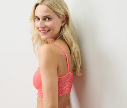 Blonde Frau lächelt über die Schulter und trägt ein Seamless-Bustier mit Spitze in Papaya.