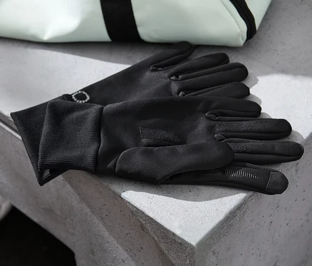 Schwarze Windprotection-Handschuhe liegen auf einer Betonfläche neben einem weißen Ball und einer Tasche.