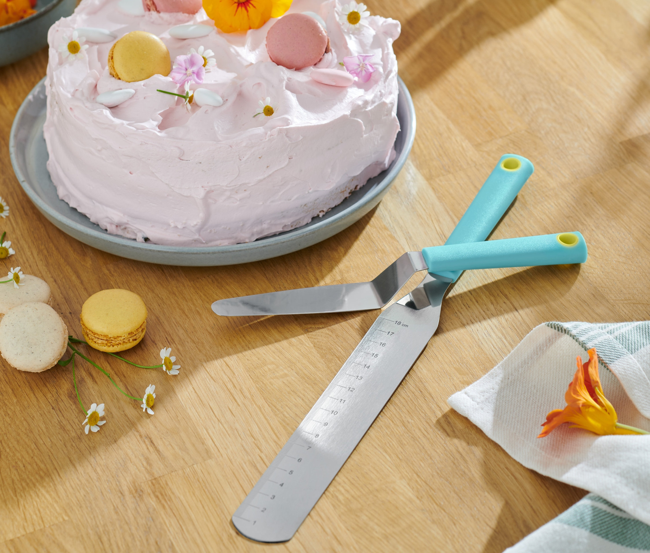Zwei sich kreuzende 2 Streichpaletten liegen auf einem Holztisch neben einem Kuchen mit rosa Zuckerguss und Makronen.