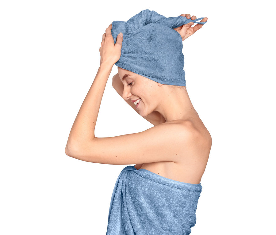 Frau wickelt ein Turban-Handtuch um ihren Kopf, ihr Körper ist mit einem Handtuch umwickelt.