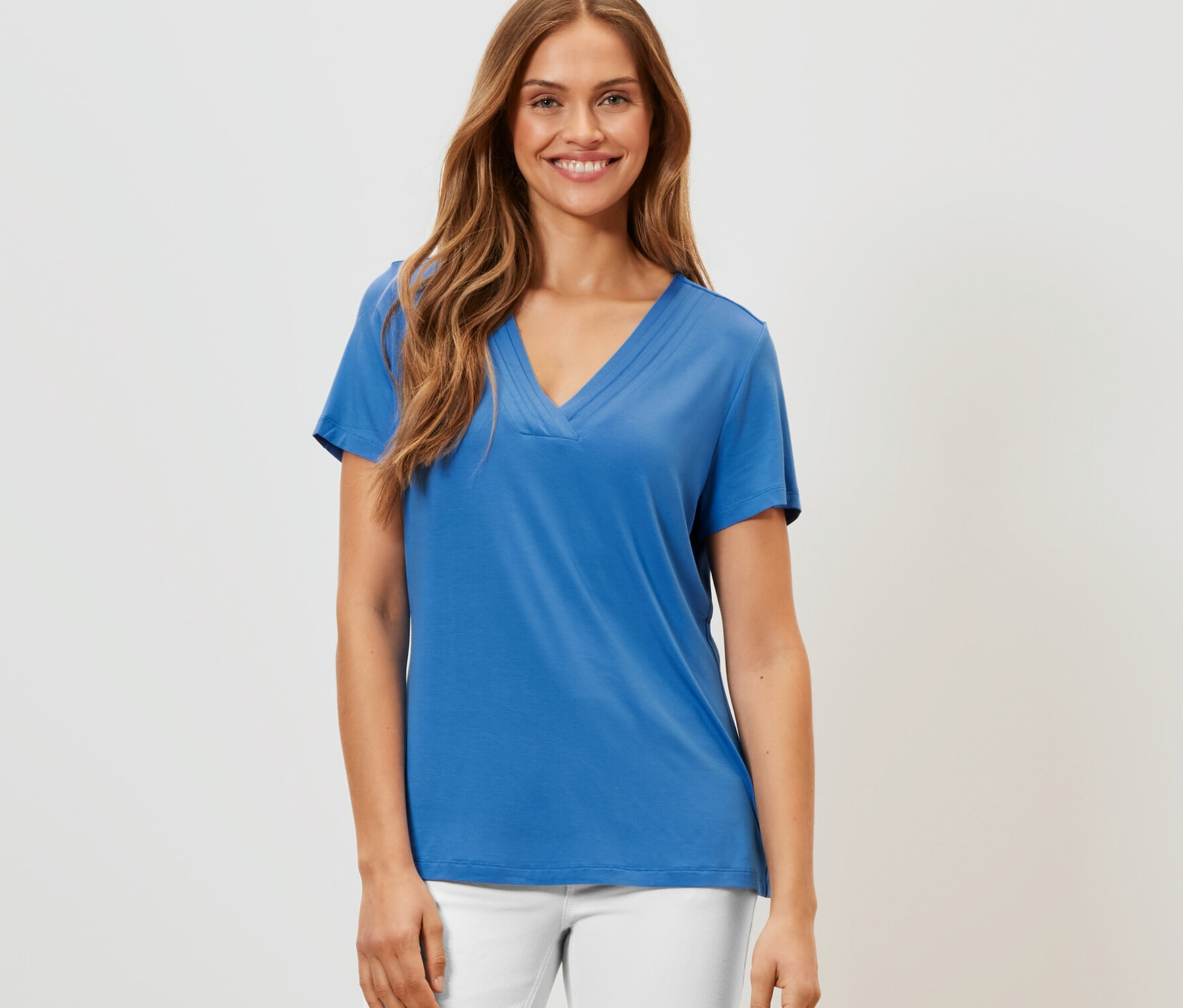 Frau trägt kobaltblaues Shirt mit Faltendetail und weiße Hose.