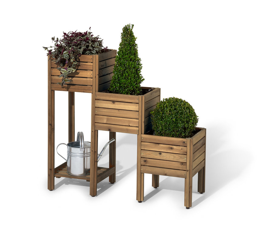 Eine hölzerne Pflanztreppe »Tinus« mit Regalboden, auf der drei Pflanzen stehen und eine silberne Gießkanne darunter.