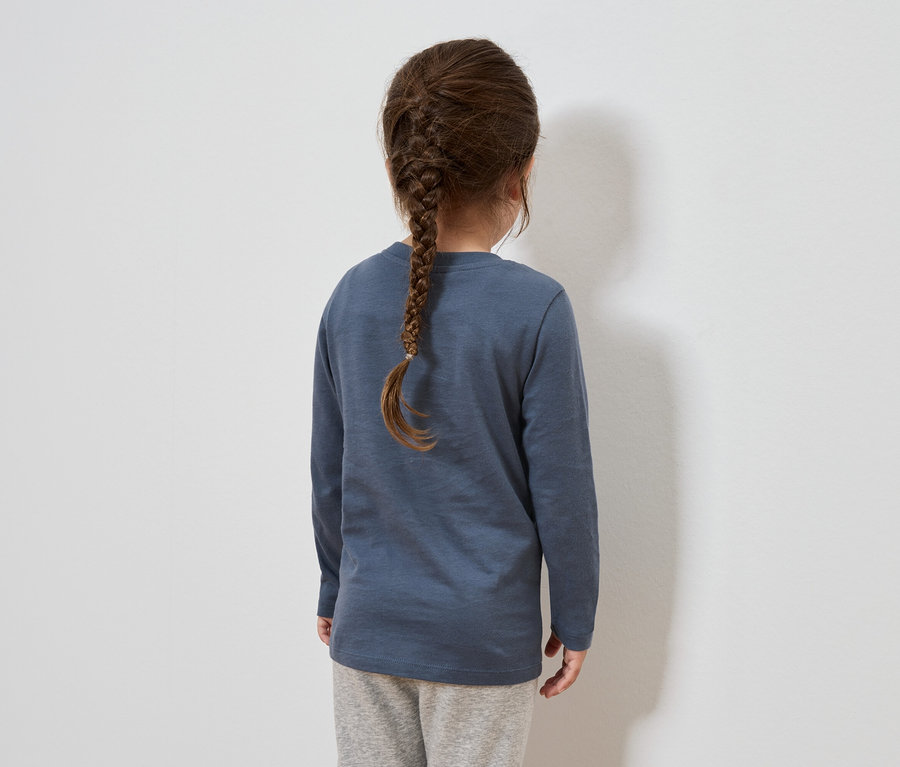 Von hinten ist ein Mädchen mit braunen, zu einem Zopf geflochtenen Haaren zu sehen. Sie trägt ein blaues Langarmshirt und eine graue Trainingshose.