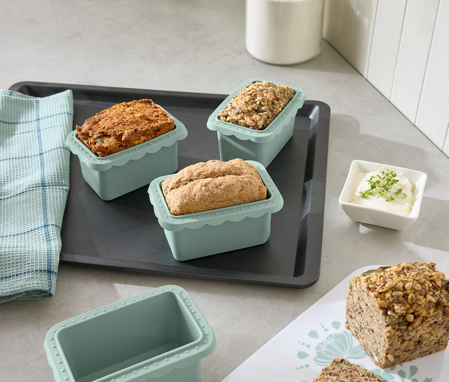 Auf einem Küchentisch stehen Mini-Backformen mit verschiedenen Brotsorten auf einem Backblech.