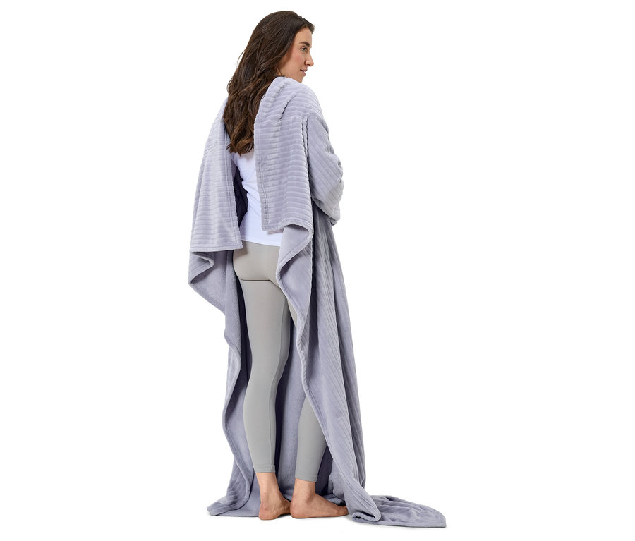 Eine Frau steht mit dem Rücken zur Kamera, eingehüllt in eine graue Decke.