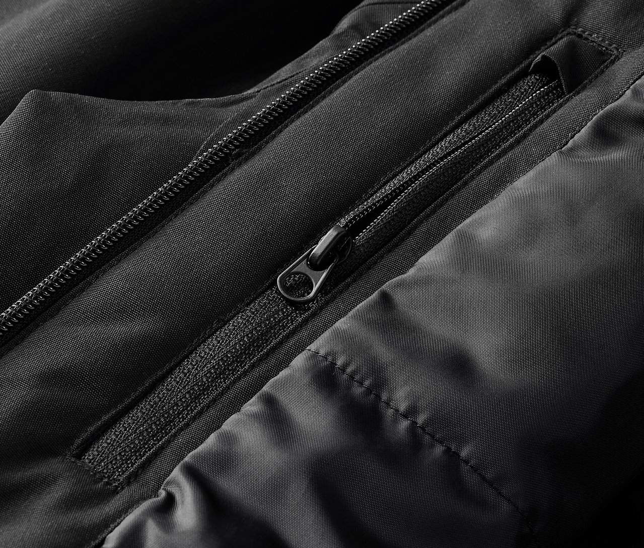 Detailaufnahme einer schwarzen Jacke mit sichtbaren Reißverschlüssen und Steppnähten.