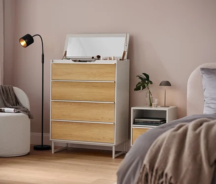 Schlafzimmer mit weißer Kommode mit vier Schubladen, Spiegel und Lampe.