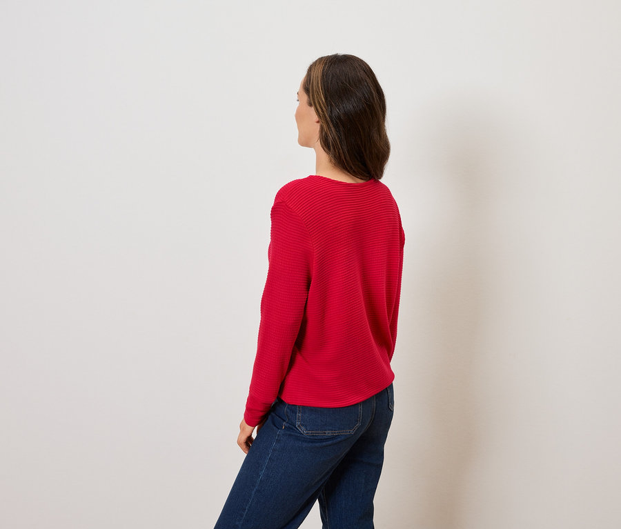 Frau schaut über die Schulter nach links, trägt einen roten Pullover und blaue Jeans.