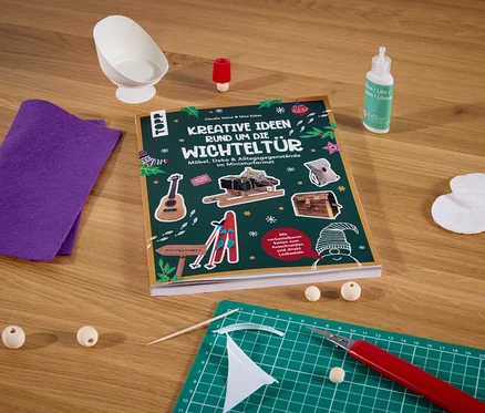 Das Buch »Kreative Ideen rund um die Wichteltür« liegt auf einem Tisch mit anderem Bastelbedarf.