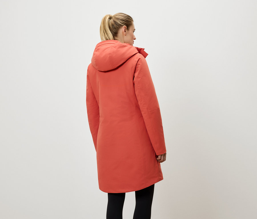 Frau von hinten trägt einen korallenroten Mantel mit Kapuze und schwarze Leggings.