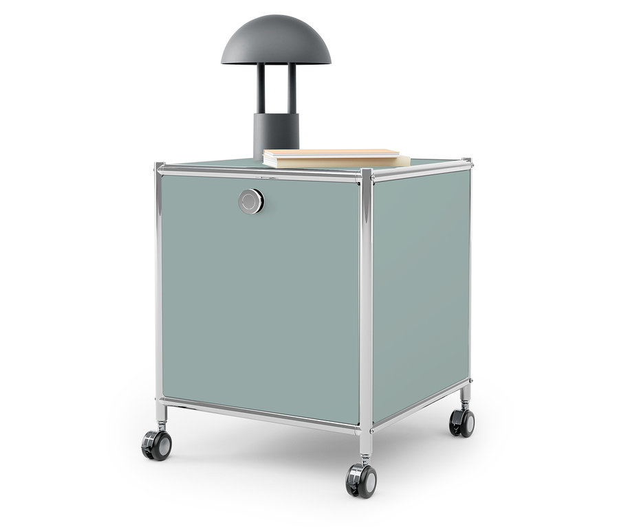 Graue Lampe und Buch auf einer blaugrünen Aufbewahrungsbox auf Rädern.