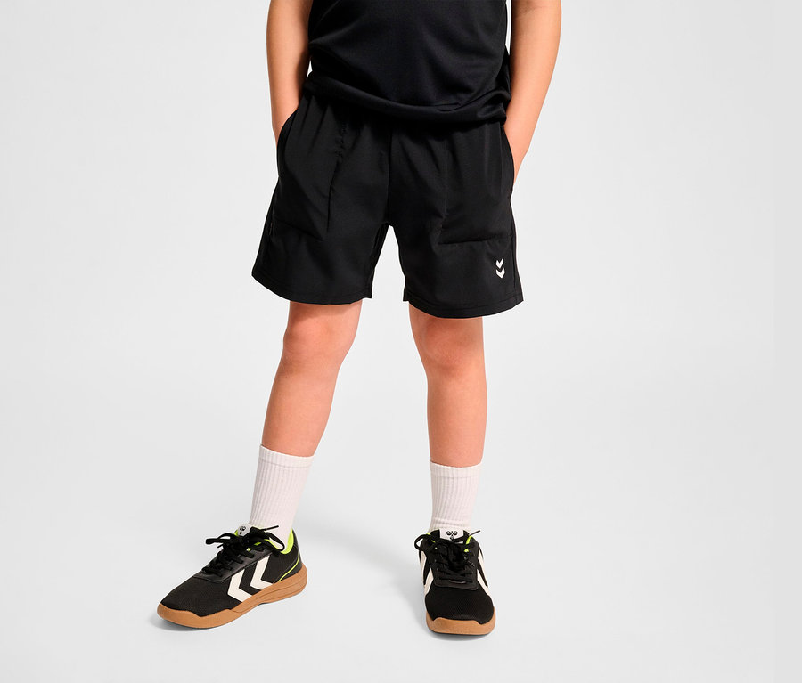 Junge trägt schwarze HUMMEL HMLJR Pulse Workout Shorts, weiße Socken und Turnschuhe.