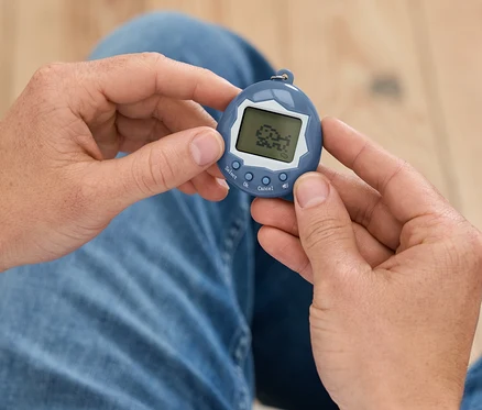 Mann hält ein blaues Tamagotchi in den Händen.