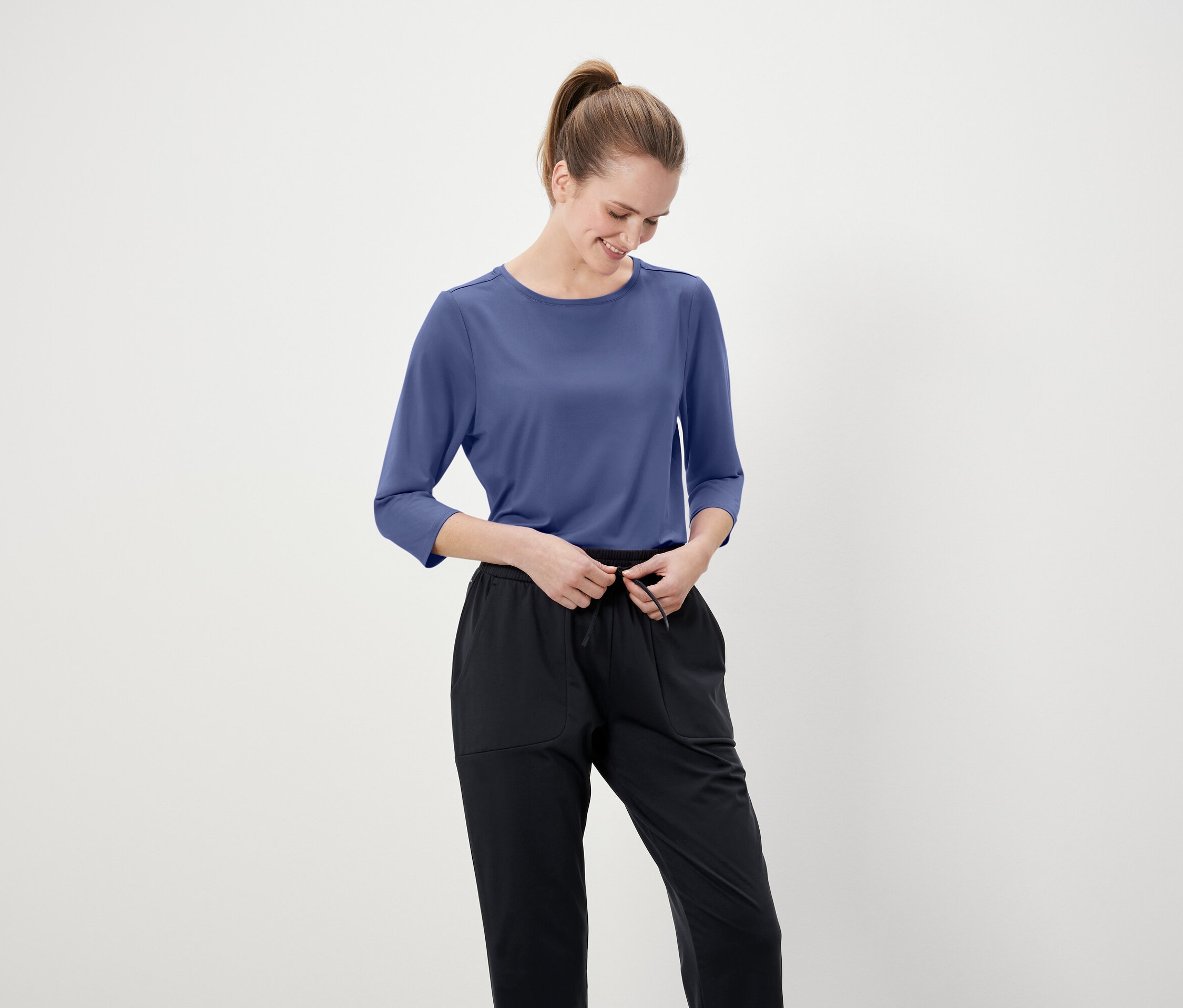 Frau justiert ihre schwarze Hose mit einem blauen Dreiviertelarm-Shirt.