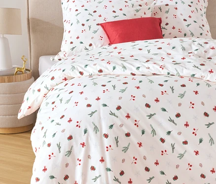 Weiße Bettwäsche mit roten und grünen Motiven und ein rotes Kissen auf einem Bett.